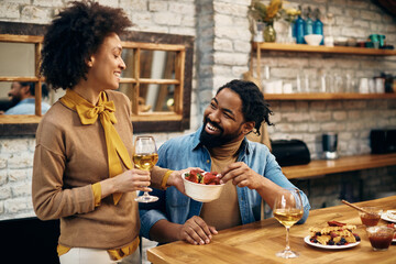 Happy African American couple enjoying in strawberries and wine at home.