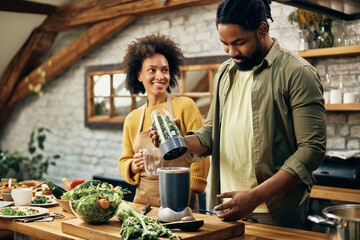 Happy black couple preparing healthy smoothie in the kitchen.