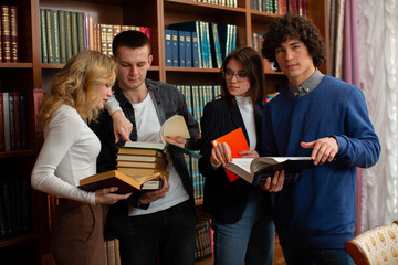 a group of students stand together in the library reading books and discussing a team project. Photos for educational sites, college advertising, schools. High quality photo