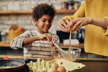Close-up of African American mother and son preparing scrambled eggs in the kitchen.