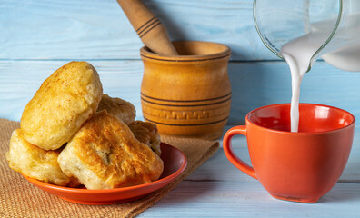 Milk is poured from a jug into an orange mug. Idea for delicious festive breakfast or dinner with milk and homemade donuts