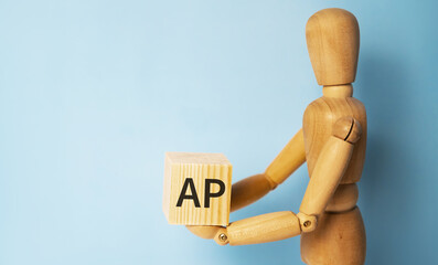 Wooden man holding a wooden cube with acronym AP-ACCOUNTS PAYABLE. Business and finances concept.