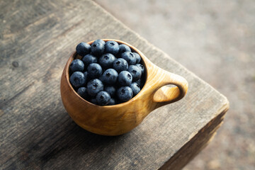 Fresh blueberries in wooden cup on wooden vintage table.
