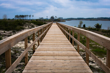 Fototapeta na wymiar Empty wooden boardwalk and handrail over grassy dune and blue cloudy sky with view over lagoon at Lagoa da Vela, Portugal