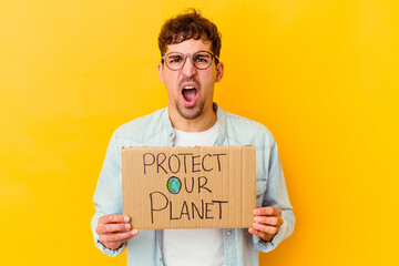 Young caucasian man holding a protect our planet placard isolated screaming very angry and...