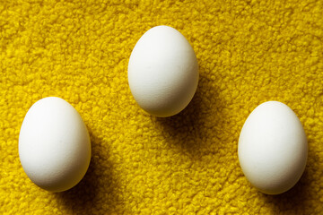 Raw eggs on a yellow background. Three eggs on a yellow fluffy surface