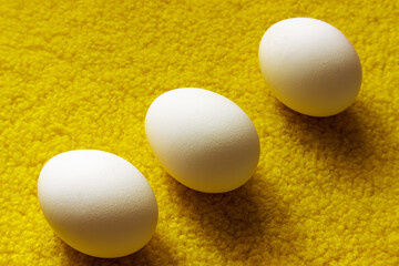 Raw eggs on a yellow background. Three eggs on a yellow fluffy surface