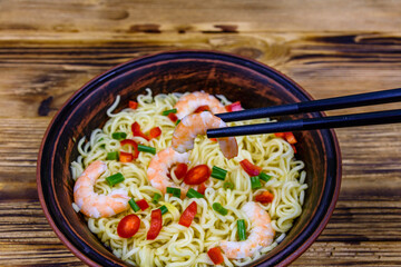 Instant noodle with shrimps, red pepper and green onion in a ceramic bowl. Japanese food. Chopsticks with shrimp