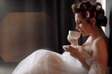 beauty portrait woman. beautiful young woman with makeup, curlerses dressed in white dress and relaxing at home holding cup of coffee or tea and looking in camera. international women's day