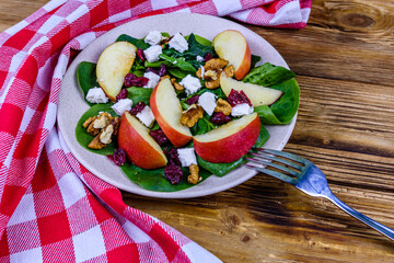 Salad with spinach leaves, feta cheese, cranberries, walnuts and apple in a ceramic plate
