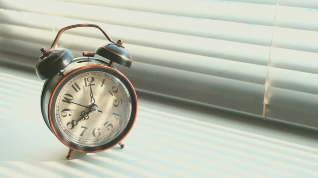 Alarm clock rings in early morning at eight o'clock in morning standing at window closed with blinds.An old vintage alarm clock rings at eight o'clock in the morning, against the blinds