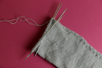 gray fabric on knitting needles on a pink background