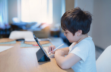 Kid using digital pen writing on tablet,Authentic Young boy using digital pad for his homework, Child studying online zoom video call with teacher, Home schooling, E-learning online education