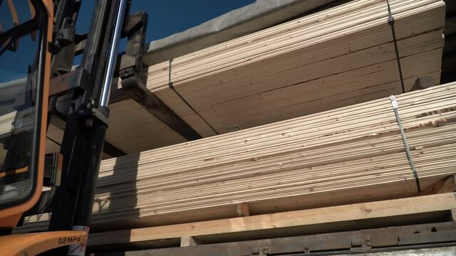 A forklift is loading wood planks into the truck. Transportation of wooden beams. Building materials for a house made of wood. Roof rafter system. Natural forestry planed products. Unloading pack.