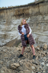 portrait of young lady with fur coat and casual cloth posing near sand rocks