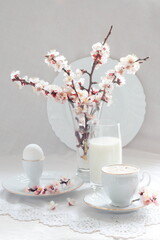 Still life with cappuccino coffee and a branch of blossoming apricot on a white background