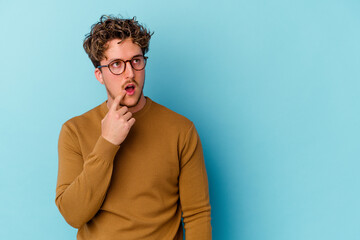 Obraz premium Young caucasian man wearing eyeglasses isolated on blue background looking sideways with doubtful and skeptical expression.