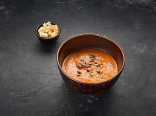Tasty vegetarian pumpkin soup in black bowl decorated with seeds on dark background