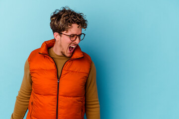 Young caucasian man wearing eyeglasses isolated on blue background shouting very angry, rage concept, frustrated.