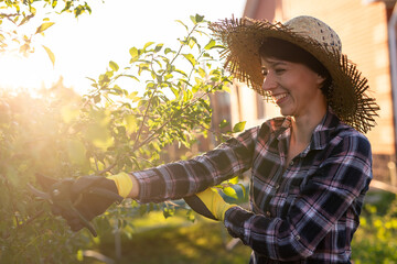 Side view of joyful young caucasian woman gardener cuts unnecessary branches and leaves from a tree...