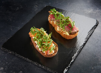Bruschetta with salmon,cherry tomatoes,fresh arugula and cream cheese on plate on dark grey black slate background
