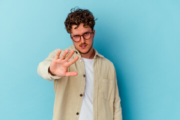 Young caucasian man wearing eyeglasses isolated on blue background rejecting someone showing a...
