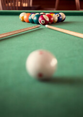 Billiard cues and colored pool balls on a gaming green cloth table, aged equipment for snooker game. Billiard sticks in playing club with a blur cue ball on a foreground.