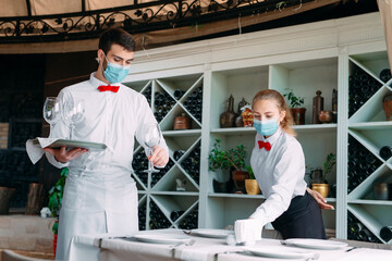 A waiter in a medical protective mask serves a table in the restaurant. Employees of a restaurant or hotel in protective masks. The End Of Quarantine.
