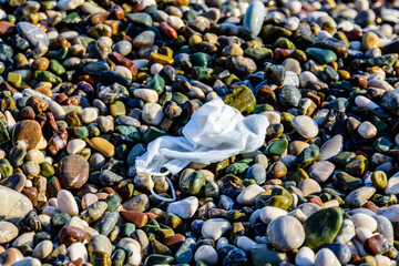 A disposable face mask discarded on pebble at the beach