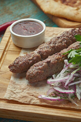 Grilled Turkish lamb lula kebab with potato, onion and rice on a wooden board. Wooden background.