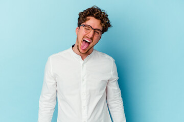 Young caucasian business man isolated on blue background funny and friendly sticking out tongue.