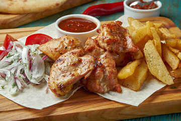 An appetizing oriental dish - grilled chicken or beef kebab with a side dish of potatoes and onions with red onions on a green background. Georgian cuisine. Shish kebab