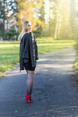 Attractive long hair girl dressed in leather jacket is  turning back to camera in autumn park. Vertically. 