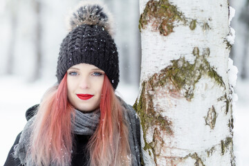 Portrait of attractive red hair girl posing next to a birch tree is smiling at the camera. Horizontally.