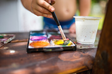 Unrecognizable boy painting outdoors in summer, close-up.