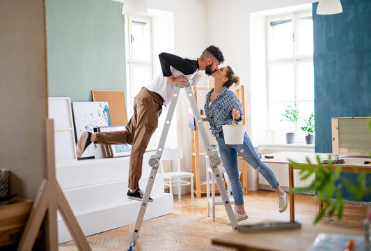 Mid adults couple kissing when painting indoors at home, relocation and diy concept.