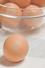 one brown egg and clear, glass. bowl of brown eggs, on a table cloth, preparing to make scrambled eggs, for breakfast