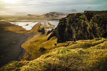 Cliffs above sea shore with flying birds during sunset at Dyrholaey in Iceland