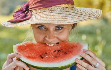 Young stylish lady in a straw hat with a bow in the park with a watermelon