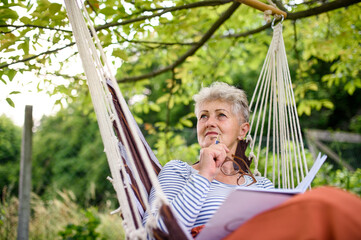 Portrait of happy senior woman sitting outdoors on hanging swing chair in garden, relaxing.