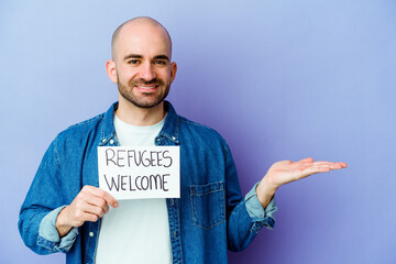 Young caucasian bald man holding a Refugees welcome placard isolated on blue background showing a...