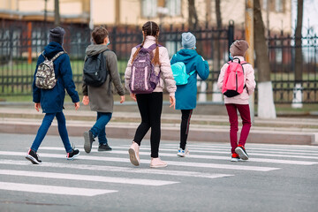 School children cross the road in medical masks. Children go to school.