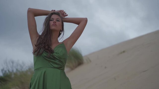 Professional dark haired women posing confidant thinkful and seductive on a sand dune beach with cloudy sky - photo shooting - cinematic slowmotion