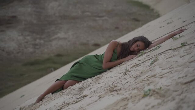 Women in an elegand classy green dress laying exhausted in a desert sand dune beach