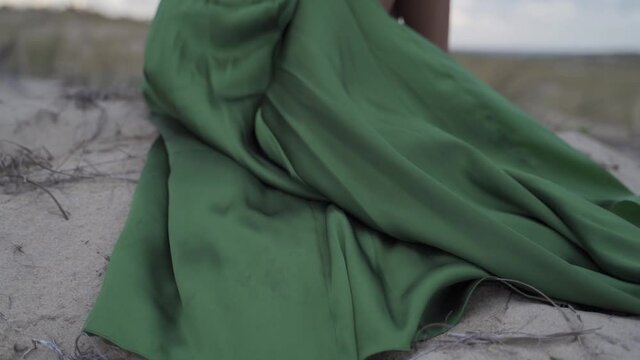Wind flying through green classy elegant dress at the sand beach windy landscape women sitting - cinematic slowmotion