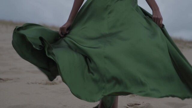 Wind blow through smaragd greend classy elegant dress while women walking at the sand beach - cinematic slowmotion
