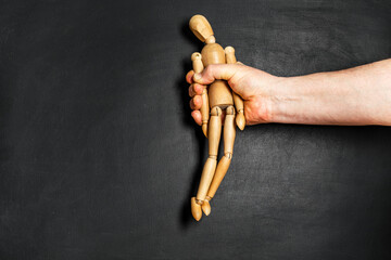 wooden man is grabbed by a man hand. The concept of helplessness and submission