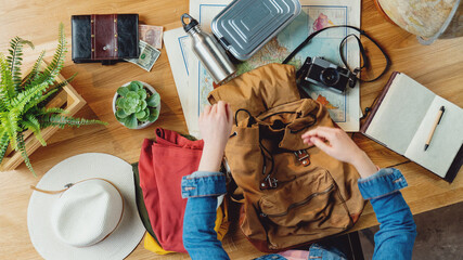 Top view of young woman packing for vacation trip holiday, desktop travel concept.