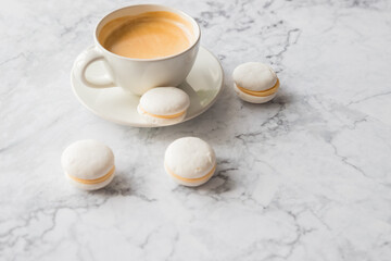 Obraz na płótnie Canvas Coffee and French macaroons on marble background.Cup of aromatic coffee cappuccino with white cookies and sprinkled grains of natural roasted coffee