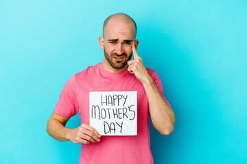 Young caucasian bald man holding a happy mothers day placard isolated on blue background showing a...